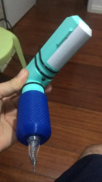 Protótipo de máquina de tatuagem verde-água com empunhadura azul e agulha, segurado na mão